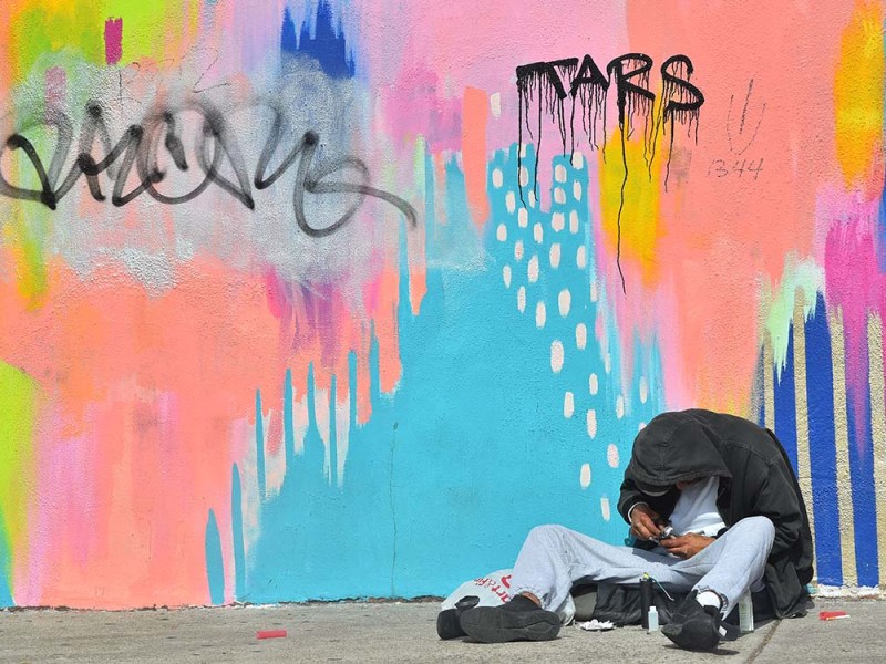 A homeless man sits against a brightly covered wall across the street from San Diego City College. Photo by Chris Stone